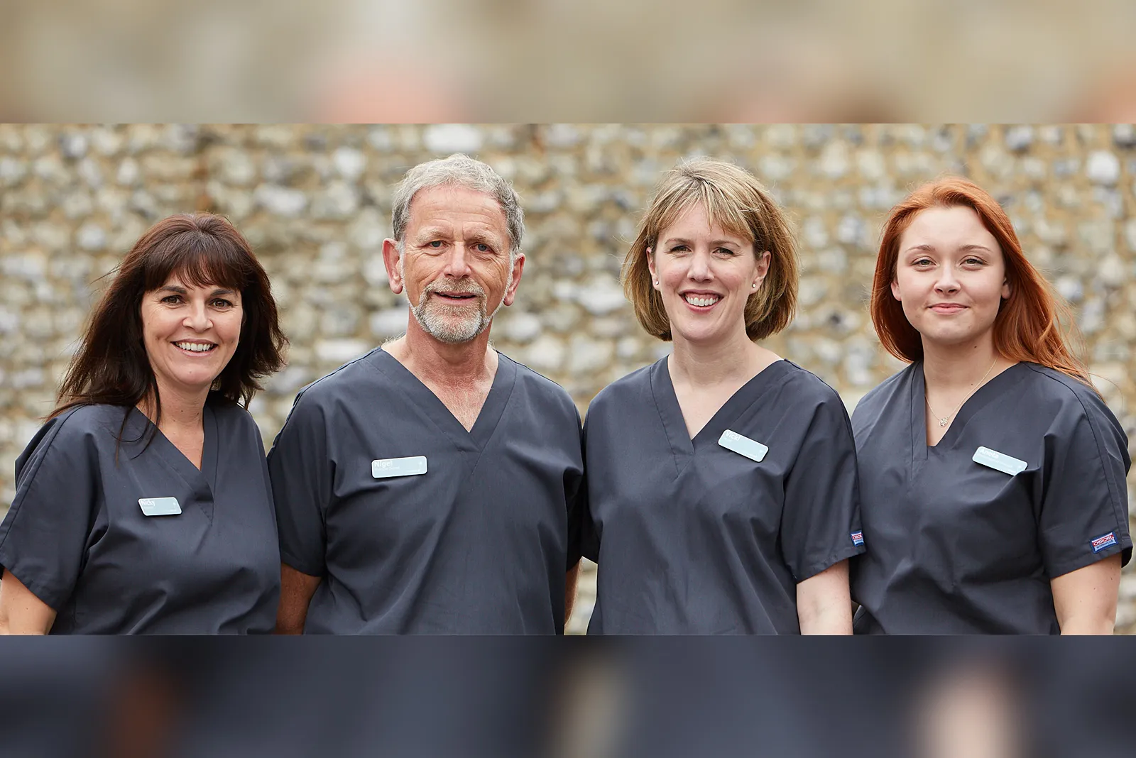 Four members of the clinical team in navy scrubs in front of a flint wall