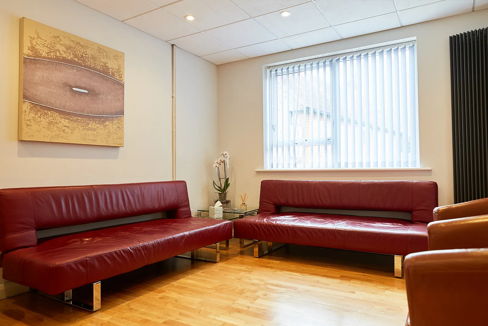 The patient lounge at South Lane Dental with red leather sofas and a wooden floor