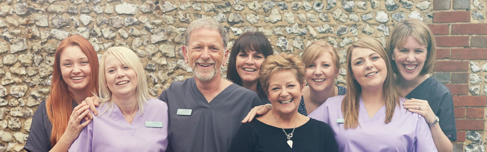 The South Lane Dental team laughing together in front of the flint wall at the practice