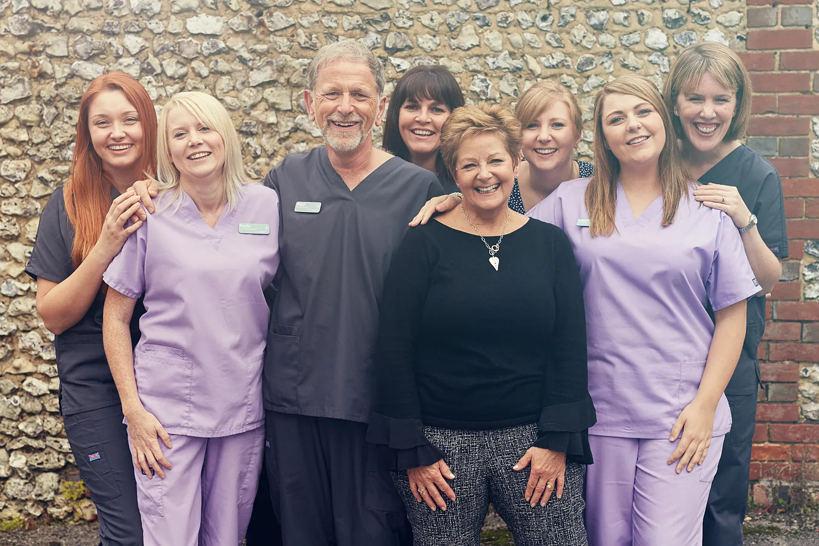 The whole South Lane Dental team standing together in front of a flint wall